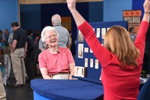 A woman laughs while the woman across the table raises her arms in a victory sign.