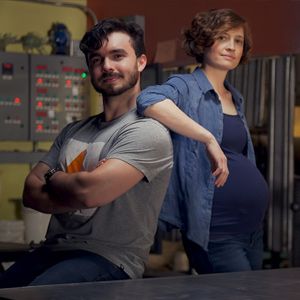 Caitlin Saks and Arlo Perez stand back to back, as she casually leans an elbow on his shoulder.